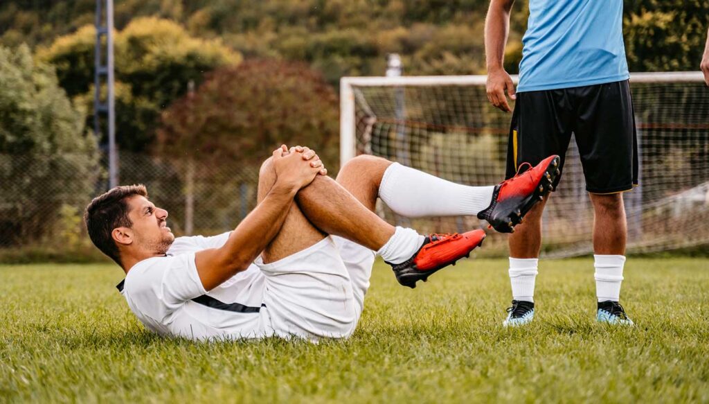 Man holding injured knee in soccer game