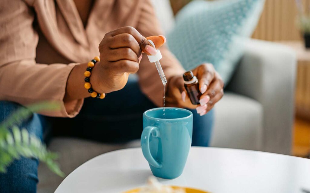 woman adding drops of CBD into drink